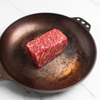 Raw steak on a cast iron skillet with a white background