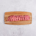 Sliced raw beef on a wooden cutting board with a light gray background