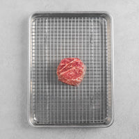 Raw Gold Plus Ribeye Filet steak on a metal wire rack over a baking sheet on a gray surface