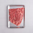Raw steak on a metal tray with a white tiled background