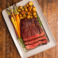 Sliced cap of ribeye steak with roasted potatoes and carrots on a white platter over a wooden background