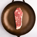 Raw NY Gold Grade™ steak with marbling on a cast iron skillet