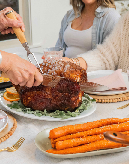 A glazed and roasted Kurobuta Ham being sliced on a table with carrots