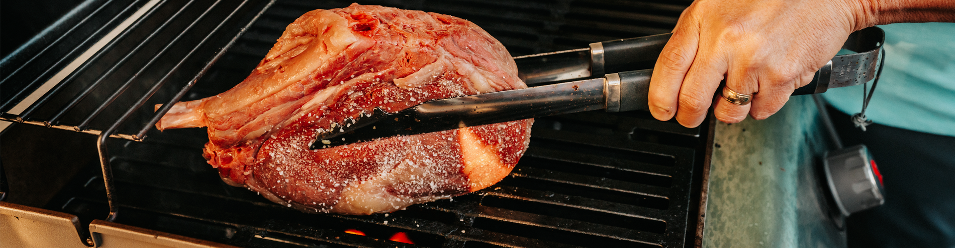 Person using tongs to handle a cowboy steak on a grill.