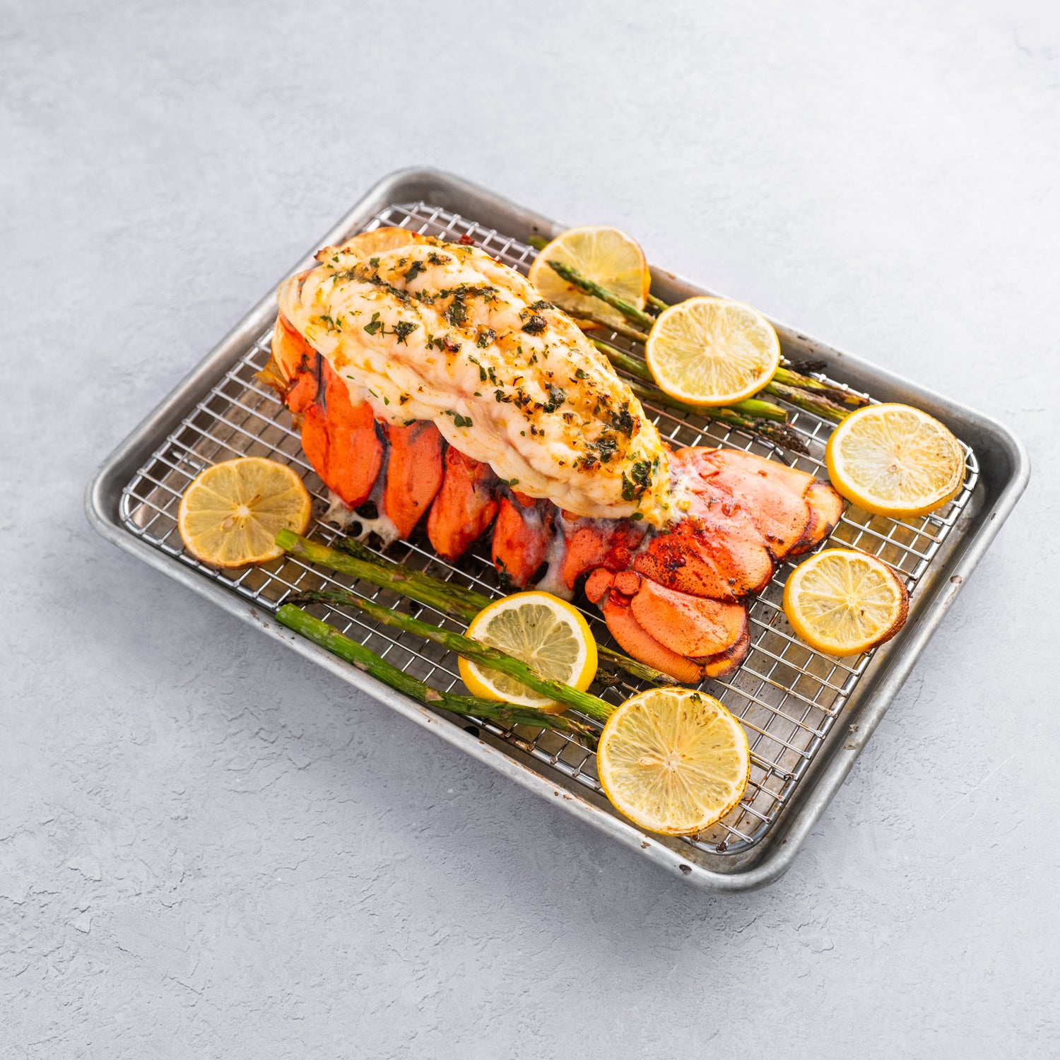 Cooked Maine lobster tail on a metal baking sheet with a white background.