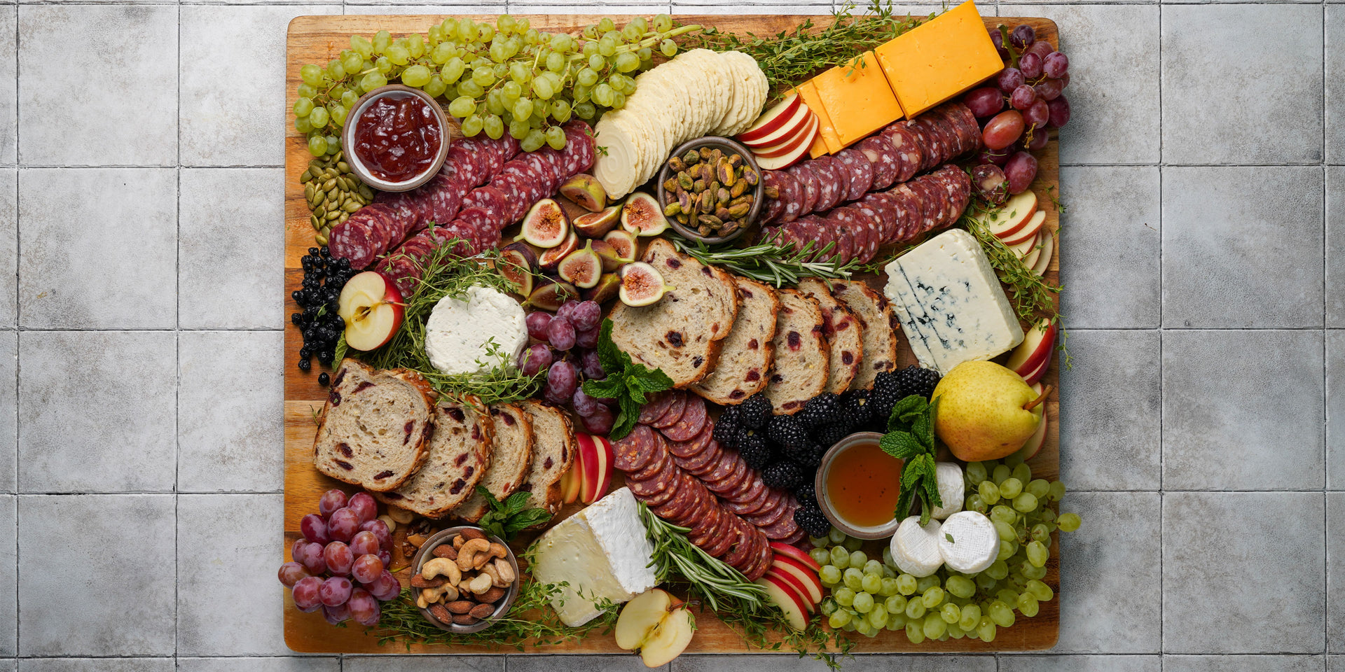 Assorted meats, cheeses, fruits, and bread on a wooden cutting board.