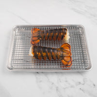 Two lobster tails on metal sheet pan with grate.