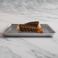 Two lobster tails on metal sheet pan with grate.