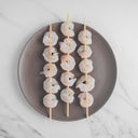 Shrimp on wooden skewers placed on plate.