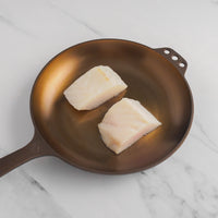 Two halibut filets on cast iron skillet.