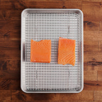 Two salmon filets on metal sheet pan with grate.