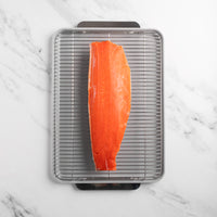 Raw salmon fillet on a metal grill rack over a marble countertop