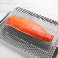 Raw salmon fillet on a metal grill rack with a white background
