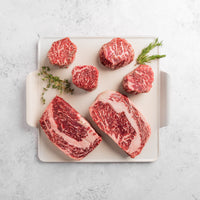 A collection of thick-cut American Wagyu steaks of various shapes and sizes, displaying a rich marbled texture.