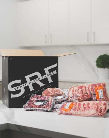 Packages of raw meat on a kitchen counter with a Snake River Farms box in the background.