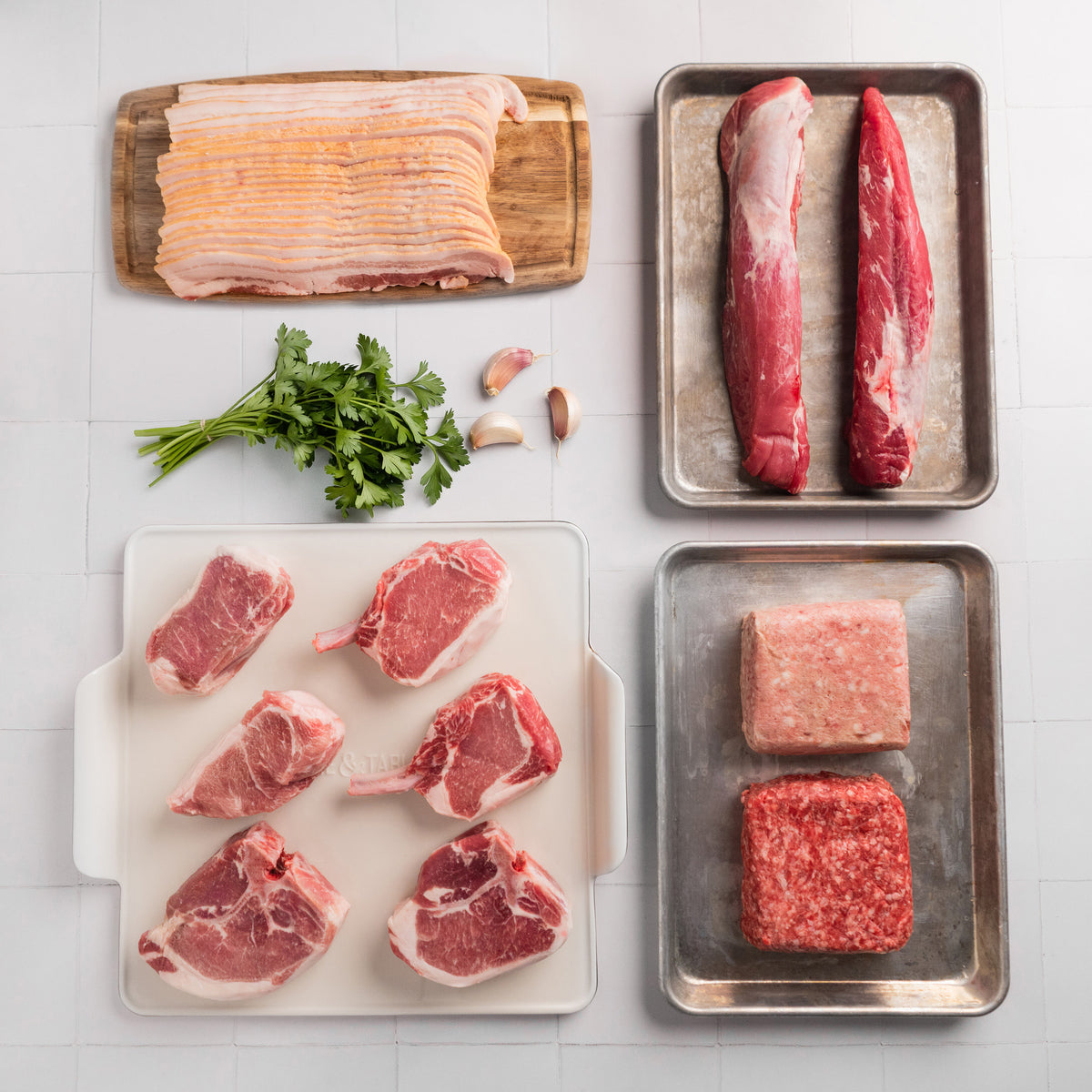 Assorted raw meats on trays with a seasoning container on a tiled surface