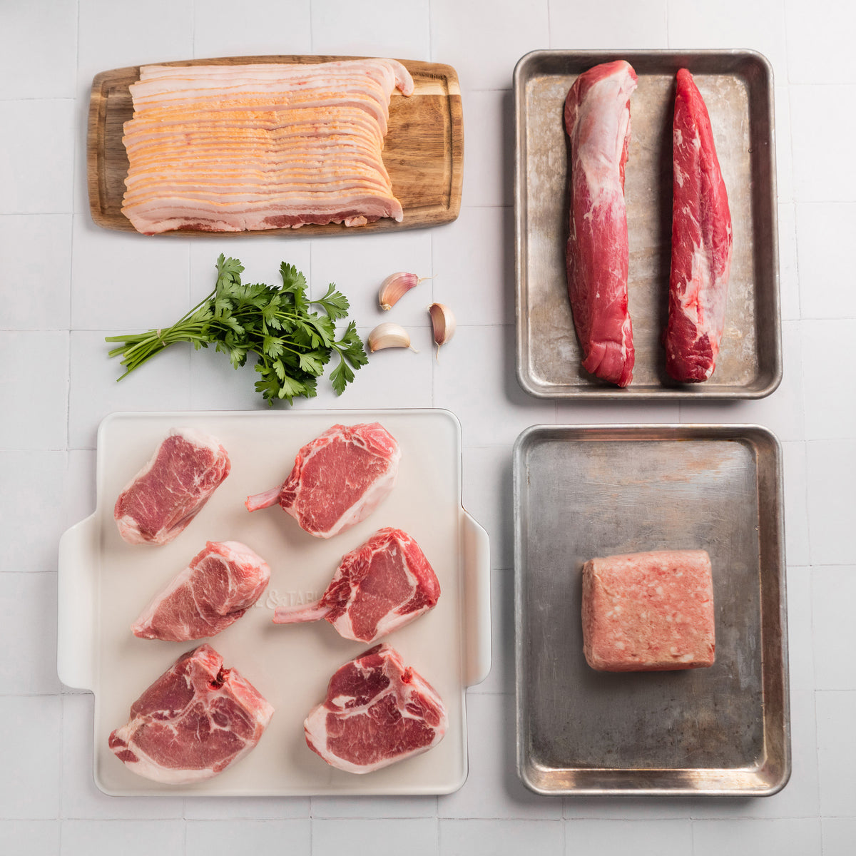 Assorted raw meats on trays with a seasoning container on a tiled surface