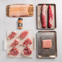 Assorted raw meats on trays with a seasoning container on a tiled surface