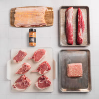 Assorted raw meats on trays with a seasoning container on a tiled surface