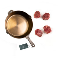 cast iron frying pan with raw beef on a white background