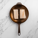 Two pieces of Northwest Pacific Cod in a cast iron skillet on a marble surface