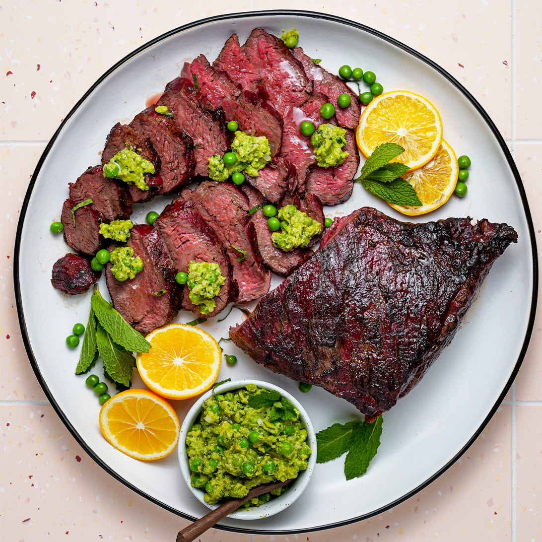 Sliced steak with green sauce and lemon wedges on a white plate