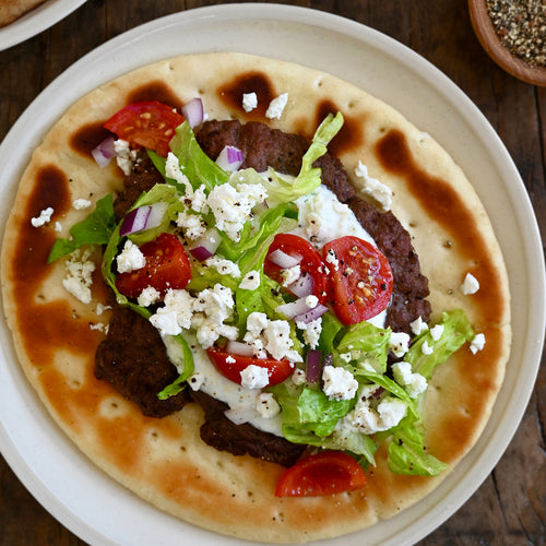 Pita bread with smash burger, vegetables, and feta cheese on a white plate.