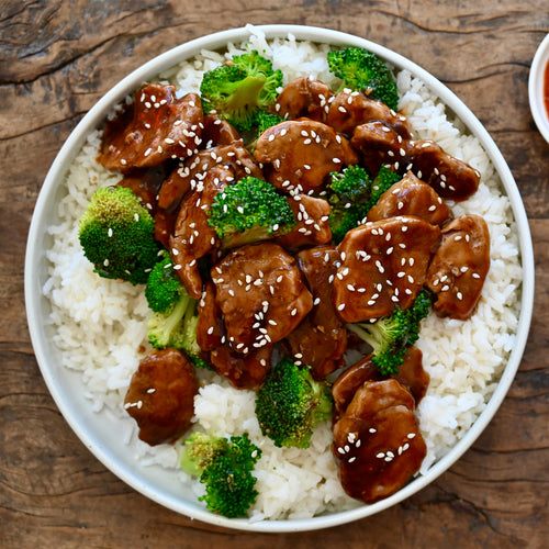 Bowl of rice with teriyaki pork and broccoli on a wooden table