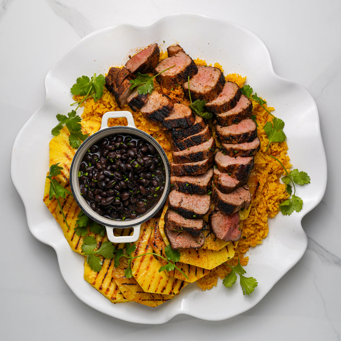 Plated dish with sliced meat, rice, beans, and tortilla chips on a white plate.