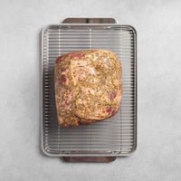 Roasted meat on a wire rack over a baking sheet on a gray surface