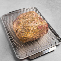 Roast beef on a metal rack over a baking tray on a gray surface