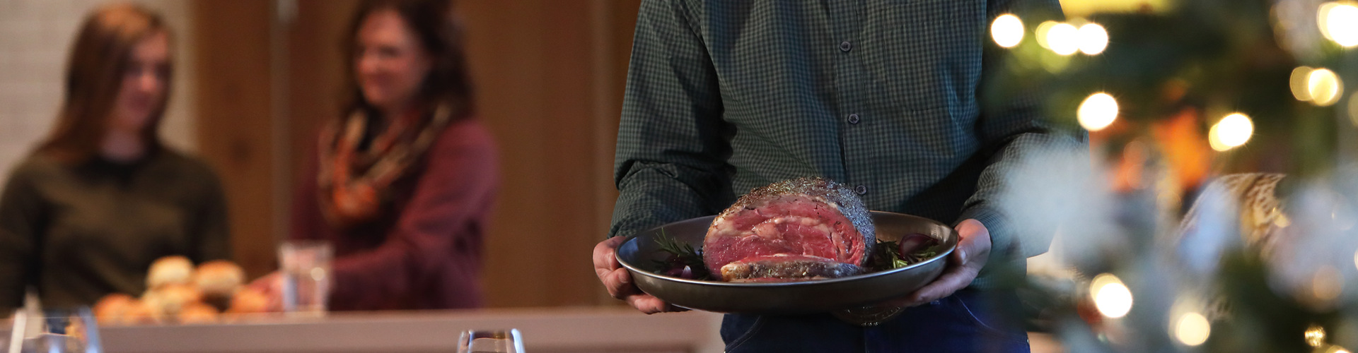 Person holding a plate with a prime rib in a festive setting with blurred people and lights.