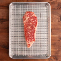 USDA Prime NY strip steak on rack and pan 