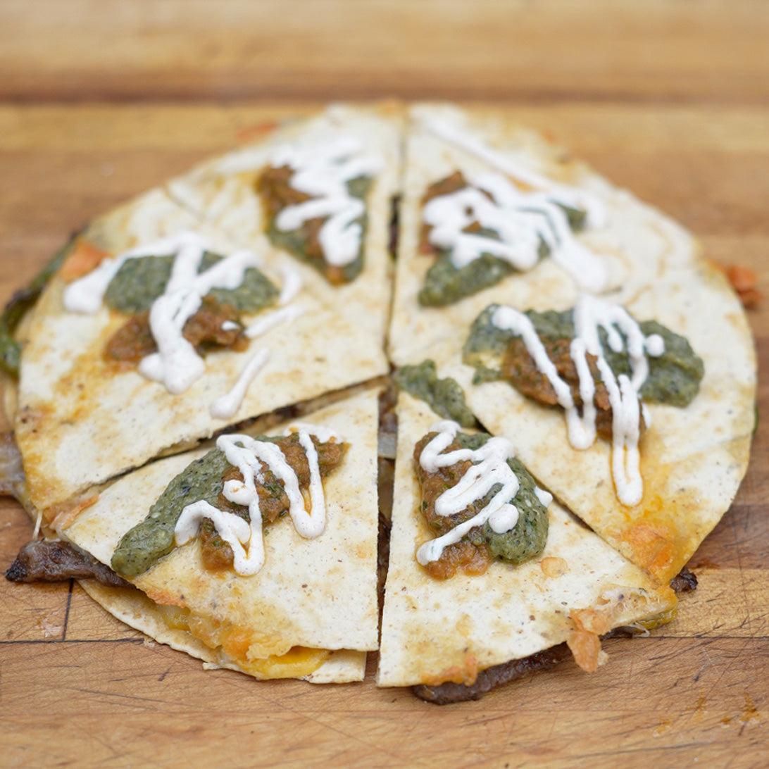 Quesadilla with green sauce and white drizzle on a wooden surface