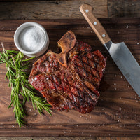 reverse seared Porterhouse steak on butcher block with knife salt and herbs