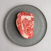 highly marbled steak on a gray plate with a light gray background