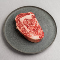 Marbled raw steak on a gray plate with a light gray background