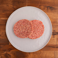 two raw patties on a white plate 