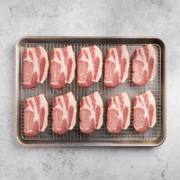 Raw Canadian bacon strips on a wire rack over a baking sheet on a gray surface