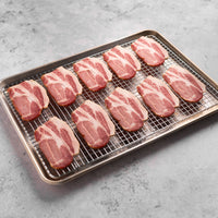 Raw Canadian bacon slices on a wire rack over a baking sheet on a gray surface