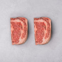 Two pieces of marbled raw beef on a gray surface