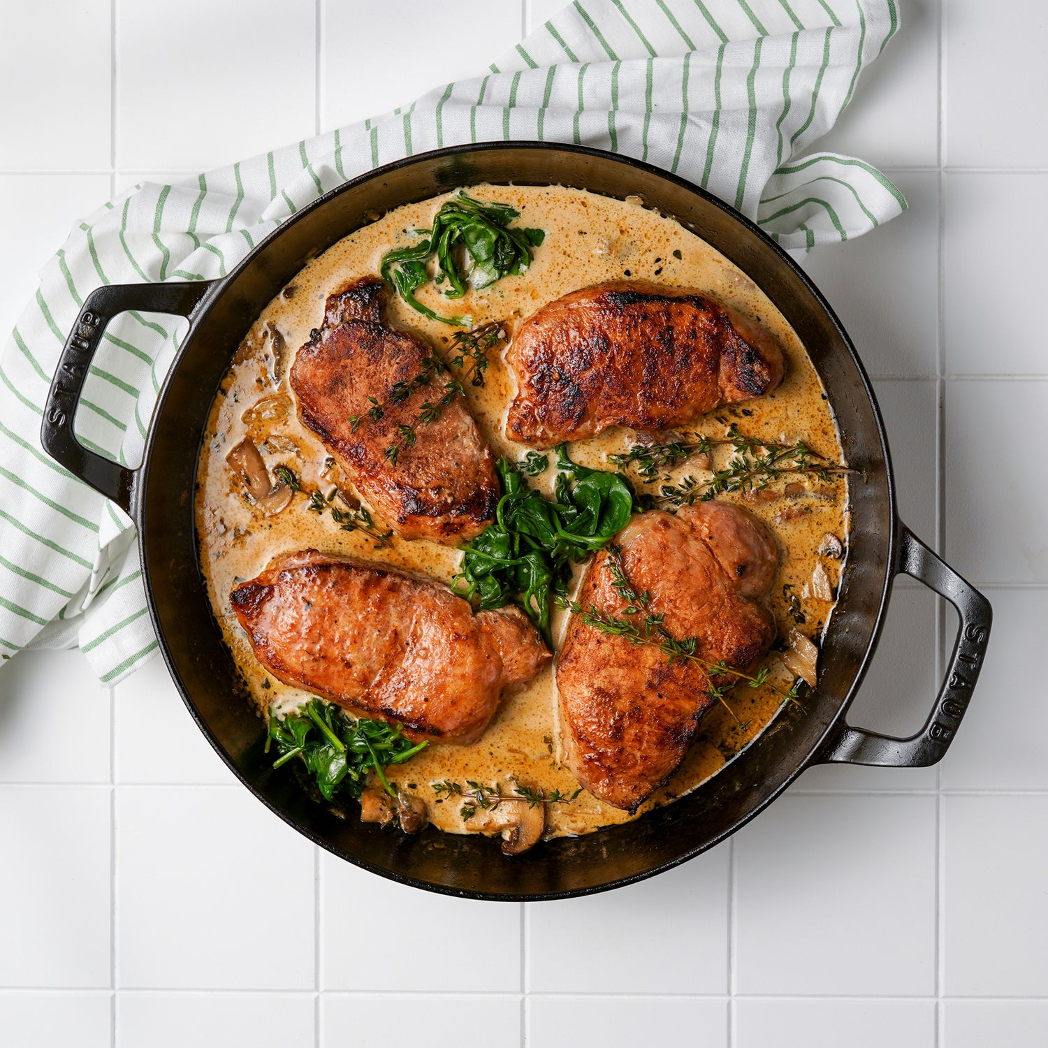 Cooked pork chop in skillet with sauce and spinach 