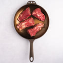 Raw beef tenderloin in a cast iron skillet on a white background