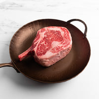 Raw ribeye cowboy steak on a cast iron pan with a marble background