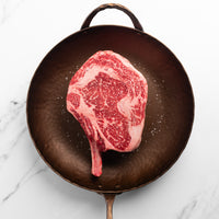 Raw ribeye steak on a cast iron skillet with a white marble background