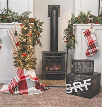 Decorated Christmas tree with lights and ornaments in front of a fireplace, with 'Snake River Farms' boxes visible.