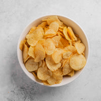 White bowl filled with potato chips on a light gray surface
