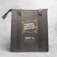Gray quilted bag with 'Pioneers of American Wagyu Beef' and 'Snake River Farms' branding on a gray background