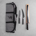 Gray knife roll with black straps and a Japanese kanji symbol, accompanied by three knives on a gray surface.