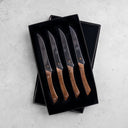 Set of four steak knives with wooden handles in a black box on a light gray surface